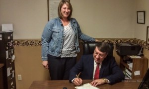 Kristi Foster-Hearing Instrument Specialist (left) and Oskaloosa Mayor Dave Krutzfeldt (right) as he signs the proclamation on Monday.