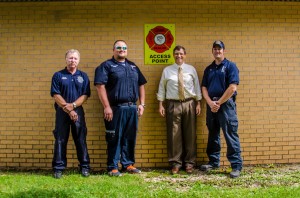 Oskaloosa Fire Captain Tim Nance (left); Mahaska County Emergency Manager Jamey Robinson (middle left); Oskaloosa Christian School Principal Dr. Bob Stouffer (middle right) and Oskaloosa Firefighter Day Hoy (right) stand in front of new signage at the Oskaloosa Christian School that will help identify where to extricate students if trapped.