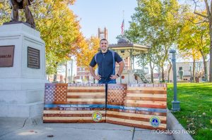 Levi Ritz poses with the 2 flags he and his wife Buffie helped to create in honor of the two fallen officers.