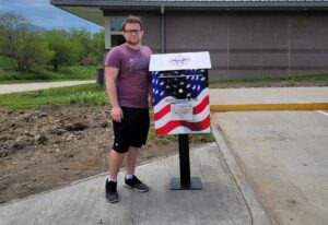 Brody Barnhart stands with one of his flag collection boxes. This one is a the Mahaska County Environmental Learning Center. The other is at the VFW facility in Oskaloosa.