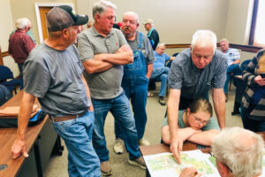 Jim Van Zomeren and his daughter Anna Schafer (right) look at a map of the airport with Jerry Searle, a planner with HDR, while other landowners discuss in the background.