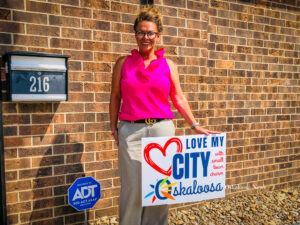 Michelle Purdum stands with one of the signs created to help create positive chatter for the Oskaloosa community.