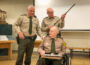 Mahaska County Sheriff Russ Van Renterghem (left), Dennis Dursky (center holding rifle), and Verlan Uitermarkt (seated) talk during a ceremony recognizing the years of service by Dursky and Uitermarkt on Sunday afternoon.