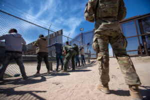  A Texas National Guardsman observes as Border Patrol agents pat down migrants who have surrendered themselves for processing, May 10, 2023. (Photo by Corrie Boudreaux for Source NM)