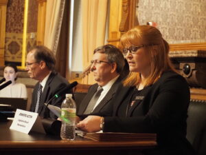  Jennifer Acton, right, director of the Fiscal Services division of the Legislative Services Agency, spoke on revenue projections for the state of Iowa at the Revenue Estimating Conference March 13, 2025. Acton is a member of the REC alongside Kraig Paulsen, center, the state budget director and Jeff Plagge, director for Northwest Bank in Spencer. (Photo by Robin Opsahl/Iowa Capital Dispatch)