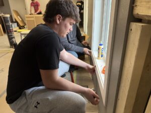 Students in the Construction Trades program gain hands-on experience as they build a house from the ground up. Senior Maddox Ashman installs light switches and outlets, Lukas Toubekis measures and trims interior finishes, and Jaden DeRonde secures cabinets. The project provides real-world skills that prepare students for careers in the construction industry.