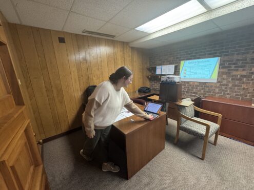 Oskaloosa High School junior Lillia Morris presents her Innovation Hub capstone project from second trimester using a projector balanced on a makeshift setup of a trash can, board, and stacked chairs, reflecting the program’s focus on creativity and problem-solving with the resources available. As the program grows, the Innovation Hub is exploring a new downtown space that better fits the needs of students and community partners.