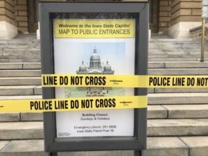  Police tape covers the sign at the visitor's entrance to the State Capitol, which was closed to the public on March 17, 2020, due to the COVID-19 pandemic. Six years later, lawmakers working to limit the governor's ability to order a variety of emergency measures during a public health crisis or other disaster. (Photo by Kathie Obradovich/Iowa Capital Dispatch)